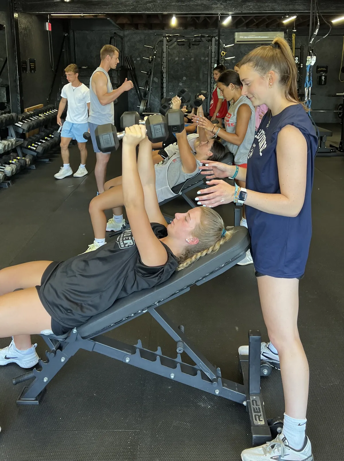 Huskies Softball athlete pressing dumbbells with a teammate spotting